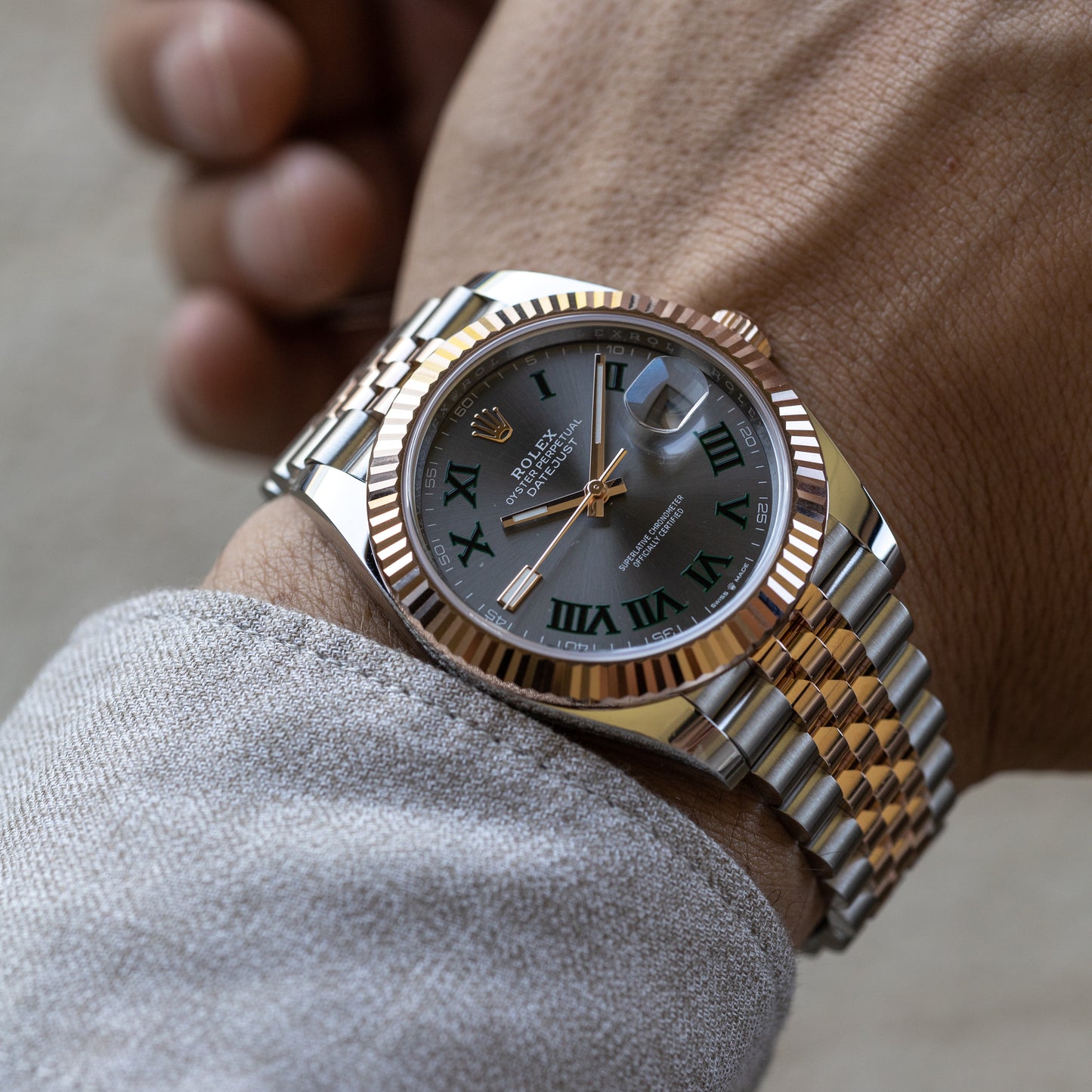 Gold and silver watch with Roman numeral dial on a wrist.