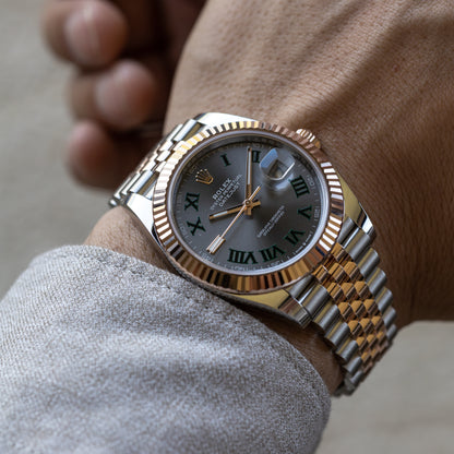 Gold and silver watch with Roman numeral dial on a wrist.