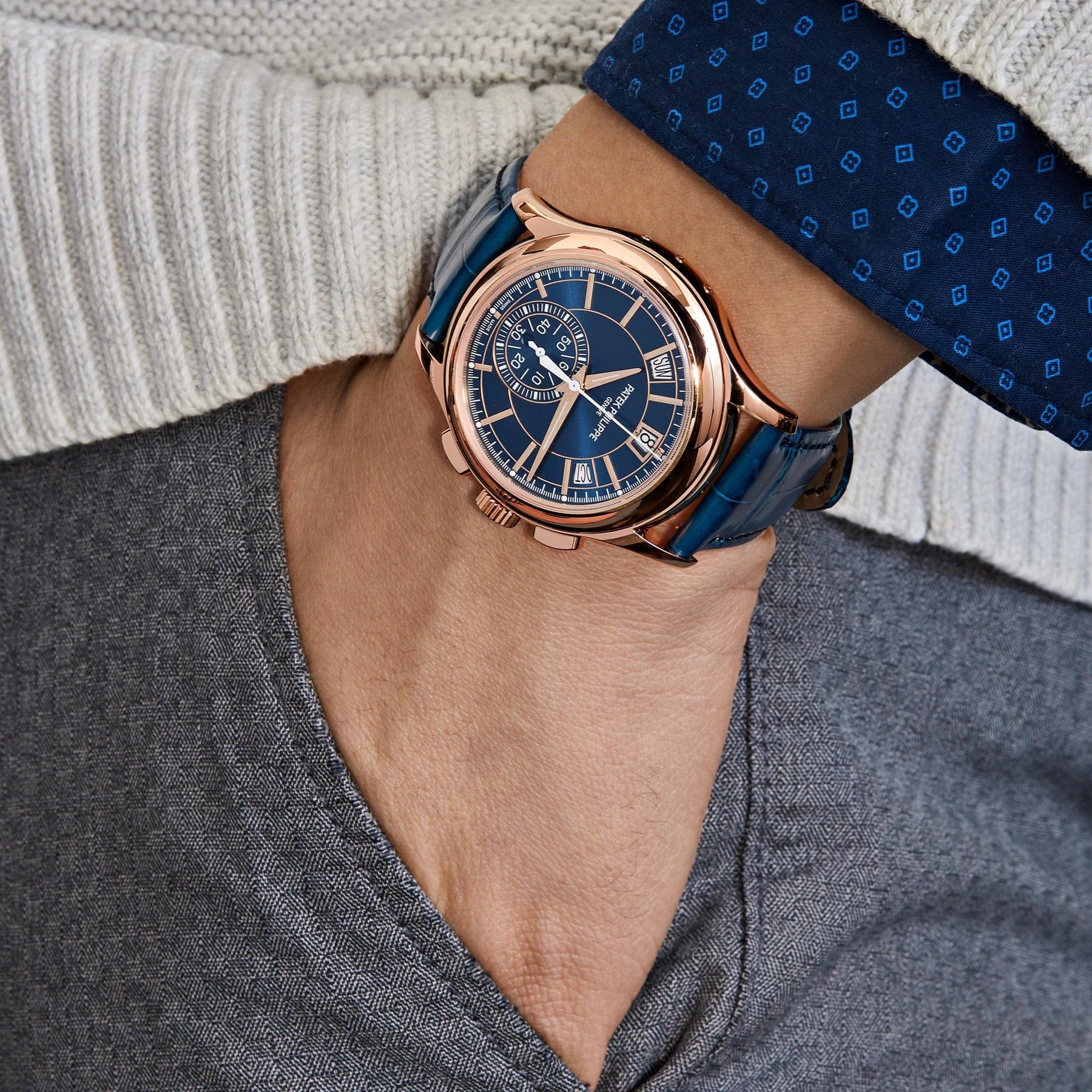 Luxury watch on a person's wrist with a blue strap and rose gold case.